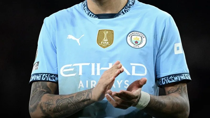 Jovem jogador brasileiro Savinho com a camisa do Manchester City em campo, olhando para a bola, com arquibancada ao fundo.