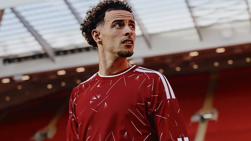 Curtis Jones fora do banco do Liverpool por precaução — Football Curtis Jones, meio-campista do Liverpool, vestindo a camisa vermelha do clube, sentado no banco de reservas durante uma partida, com expressão séria.