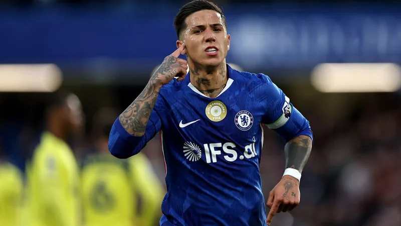 Enzo Fernández vestindo o uniforme do Chelsea, aquecendo na beira do campo, com o estádio Stamford Bridge ao fundo durante uma partida noturna.