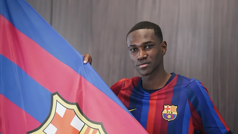 Josué Caicedo reforça Barcelona B por empréstimo — Football World Cup Jovem jogador equatoriano Josué Caicedo vestindo a camisa do Barcelona B, sorridente, em campo de treinamento, com o escudo do clube ao fundo.