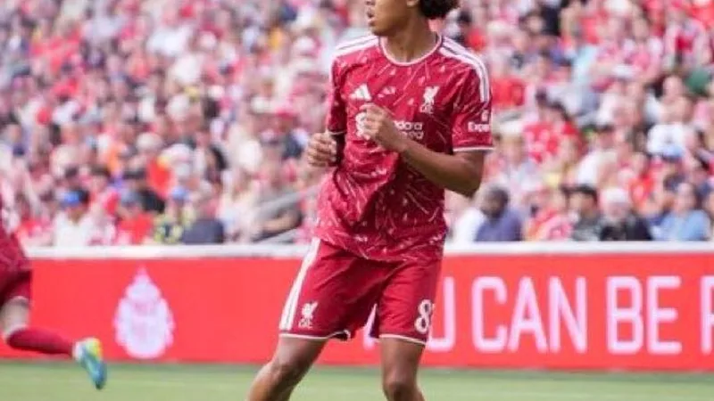 Jovem atacante nigeriano Ifeanyi Ndukwe com a camisa do Liverpool durante treino, em campo de futebol, com bola nos pés e olhar determinado.