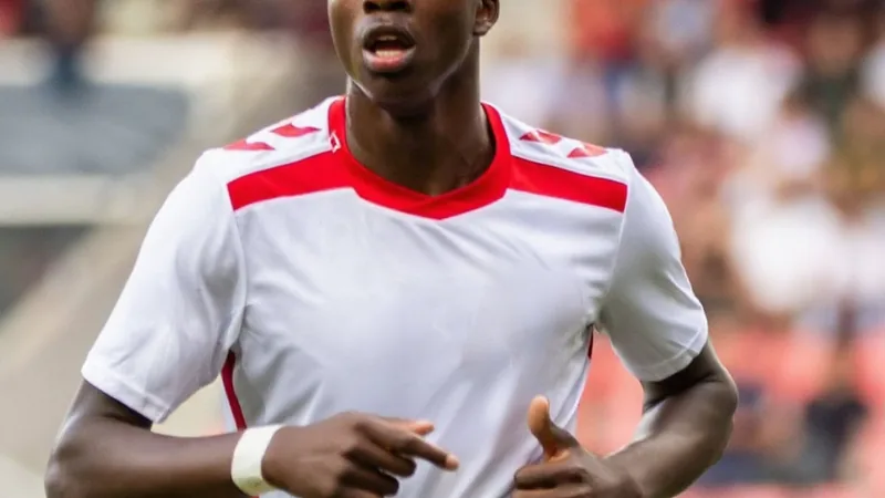 Jovem atacante Mansour Ouro-Tagba vestindo a camisa do VfL Bochum durante apresentação oficial no estádio, com fundo do gramado e torcedores ao longe.